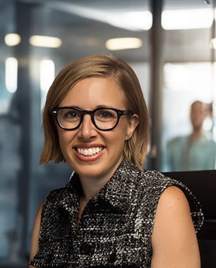 Profile photo of a young woman with an office setting in the background (Photo)